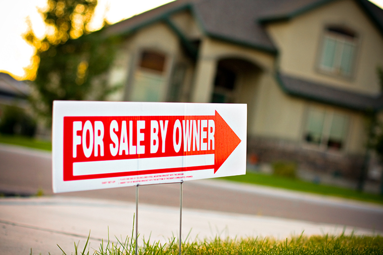 a For Sale By Owner sign in a front yard